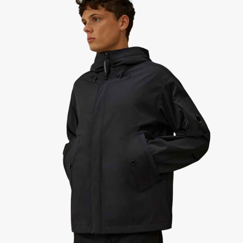 Veste technique noire de CP COMPANY en collaboration avec RÆW DISTRICT, avec design moderne et détails techniques visibles.