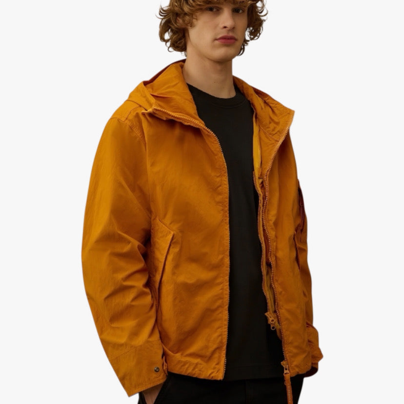 Veste orange de CP COMPANY en collaboration avec RÆW DISTRICT, vue de face, avec détails du tissu et fermeture éclair visible.